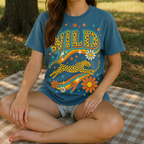Woman wearing a blue t-shirt with a 'Wild' design sitting on a blanket outdoors.
